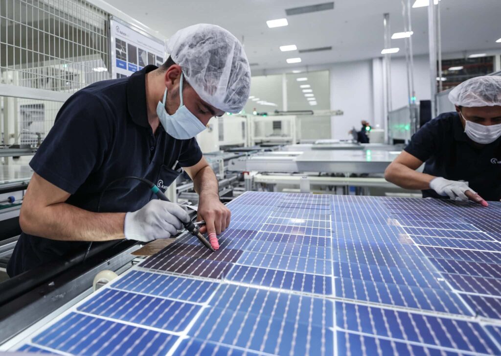 “Technicians assembling high-efficiency solar cells on photovoltaic panel production line in manufacturing facility”